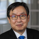 Andrew Shiotani smiles slightly in a headshot. He wears black glasses and a bright blue tie with a black coat.